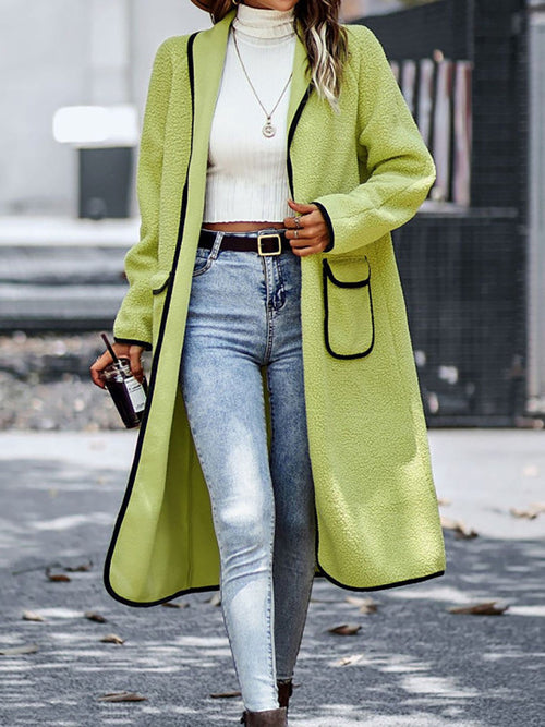 Bright green long sleeve coat with pockets and a classic collar worn over a white top and blue jeans.