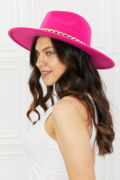 Stylish bright pink fedora hat with studded details worn by a smiling woman with long wavy brown hair.