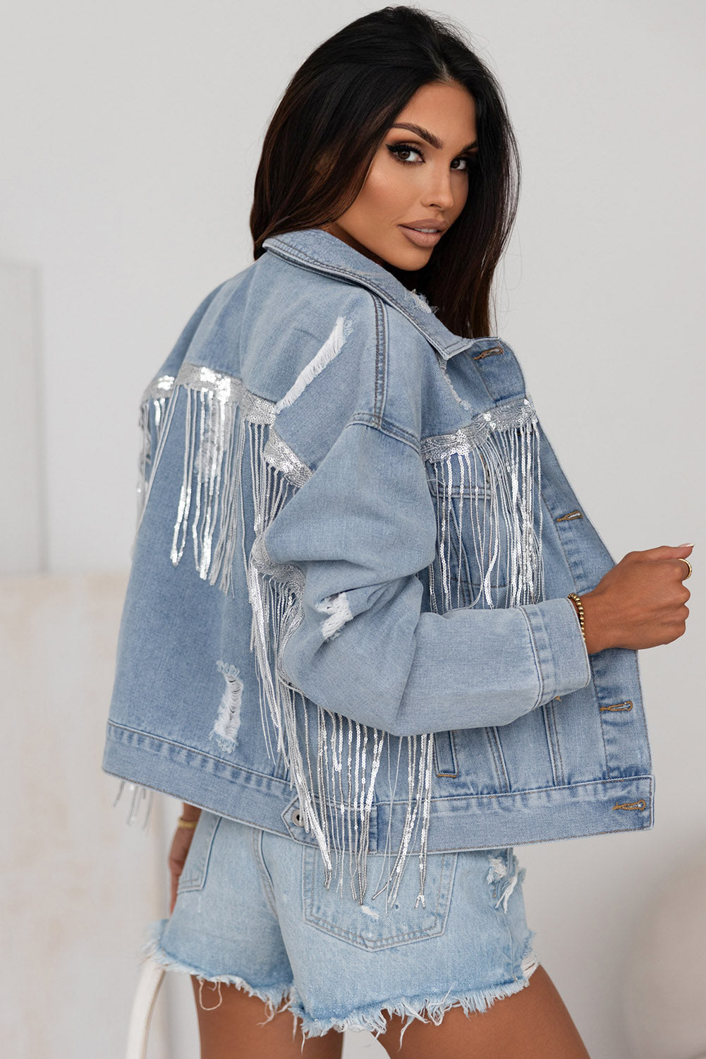 Sequin-trimmed distressed denim jacket with fringe detail, showcased on a model against a white background.