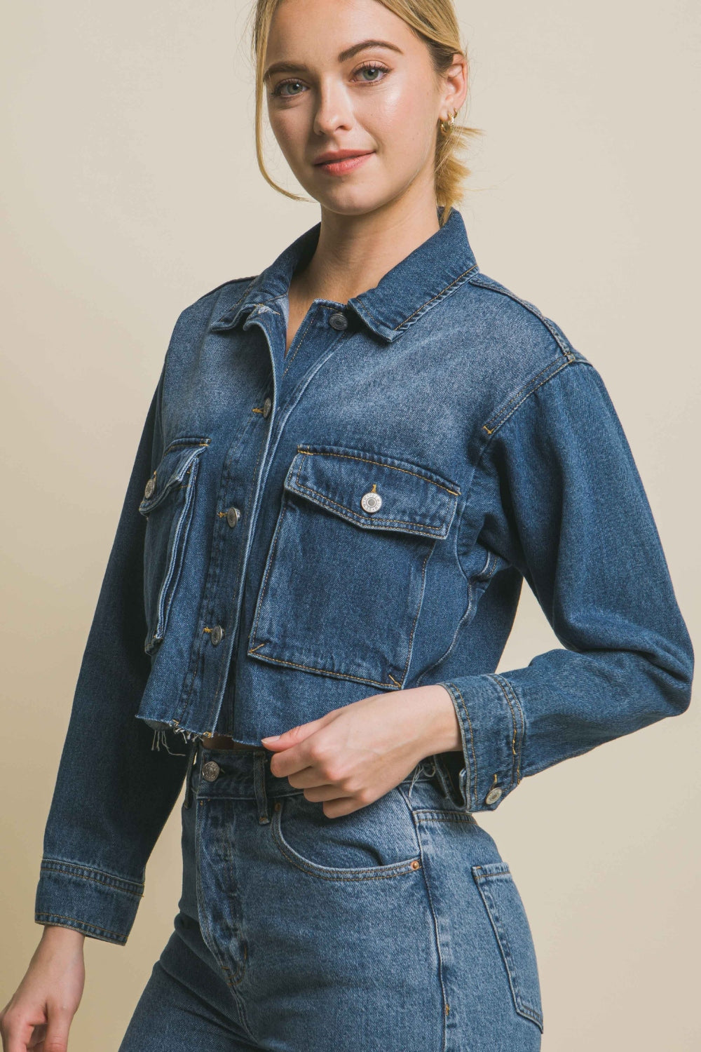 Raw hem cropped denim jacket with button-up closure, modeled by a young woman with blonde hair against a neutral background.