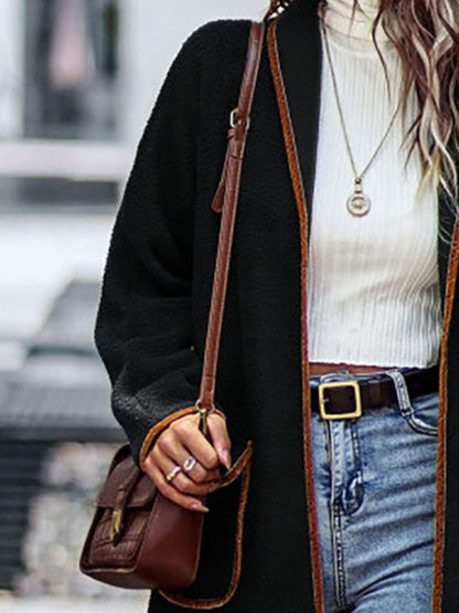 Elegant long sleeve coat with contrast trim and pockets, paired with a white top, blue jeans, and a brown leather handbag.