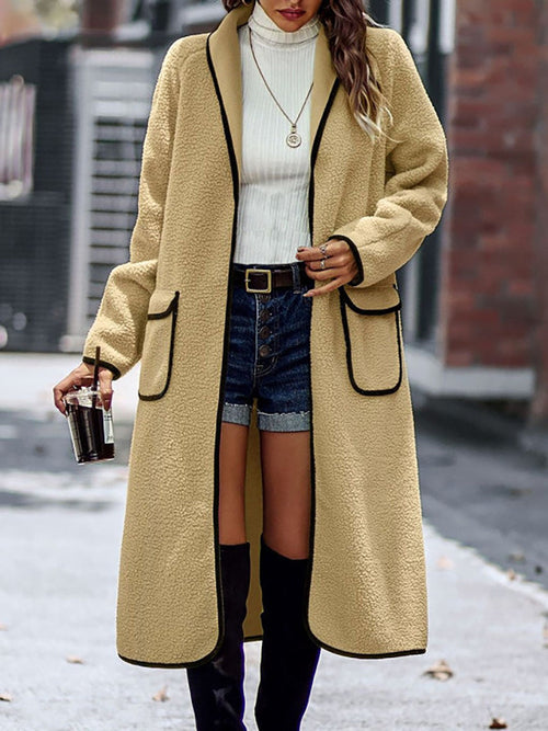 Warm, oversized long sleeve beige coat with contrast trim and pockets worn by fashionable woman on city street.