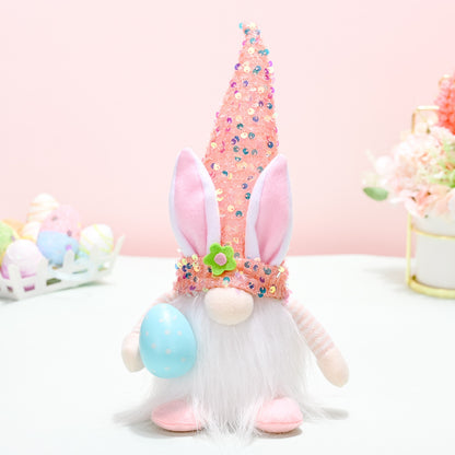 Colorful Easter Sequin Gnome Hat
A whimsical Easter-themed gnome figurine sporting a tall, sequin-covered hat with bunny ears and a fluffy white beard. The gnome is sitting on a light-colored surface, surrounded by small decorative eggs in pastel colors.