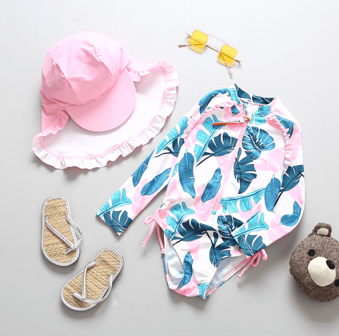 Colorful tropical printed women's swimsuit, pink ruffled sunhat, and straw sandals - a stylish summer beach outfit displayed on a white background.