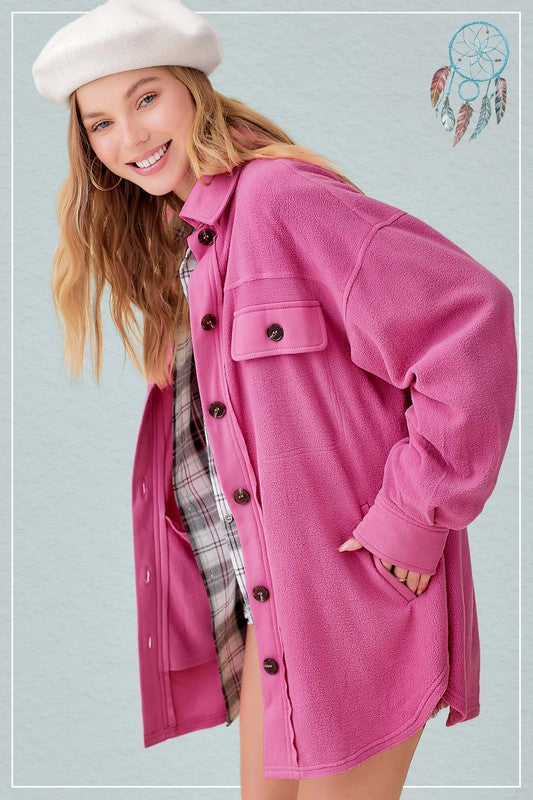 Smiling woman in a bright pink woolen jacket, styled with a white beret, stands in front of a background with a dreamcatcher motif.