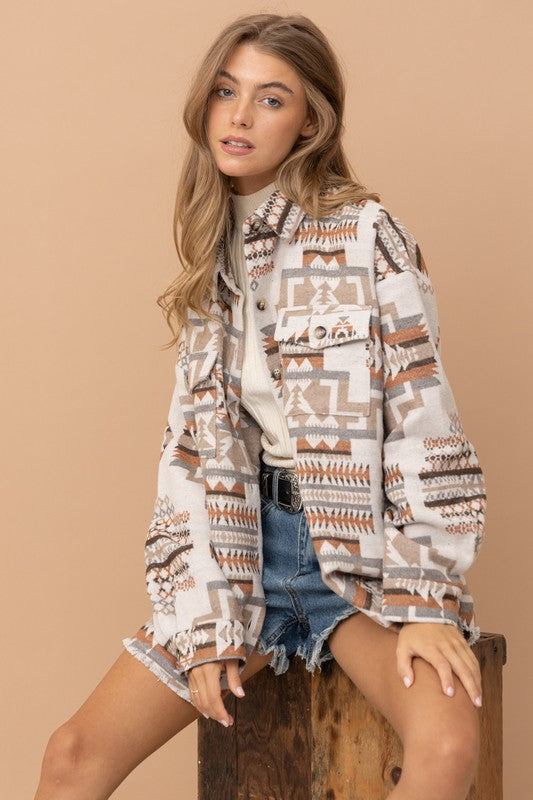 Airy Aztec-inspired shacket with frayed edges, featuring a bold graphic pattern in neutral tones, complementing the casual denim shorts.