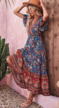 Floral printed maxi dress with bohemian design, strappy V-neck, and intricate pattern in a colorful palette, worn by a young woman posing in a tropical setting.