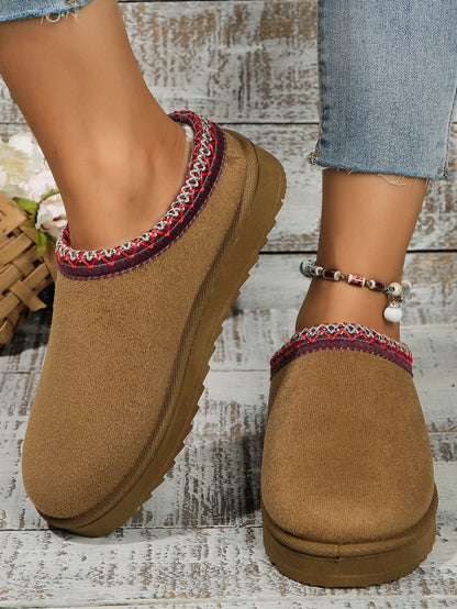 Textured tan platform slippers with colorful embroidered trim, showcased on a rustic wood surface.