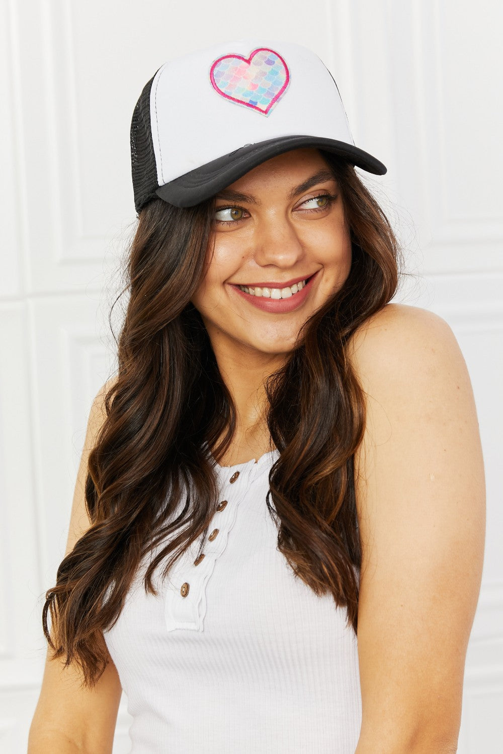 Stylish woman wearing a trendy heart-patterned trucker hat, smiling confidently.