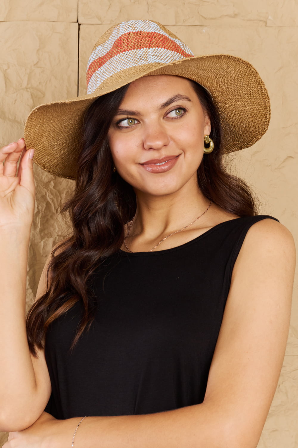 Elegant straw sun hat with vibrant stripes, worn by a smiling woman with flowing hair against a neutral background.