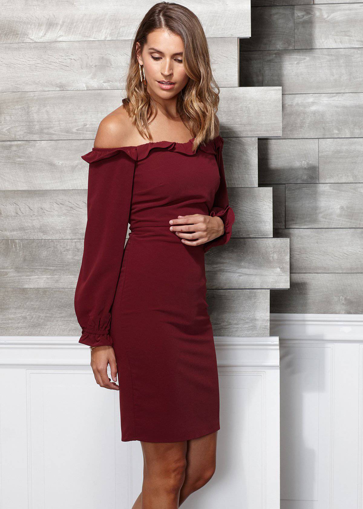 Elegant off-shoulder bodycon dress in rich burgundy, worn by a stylish woman against a modern concrete backdrop.