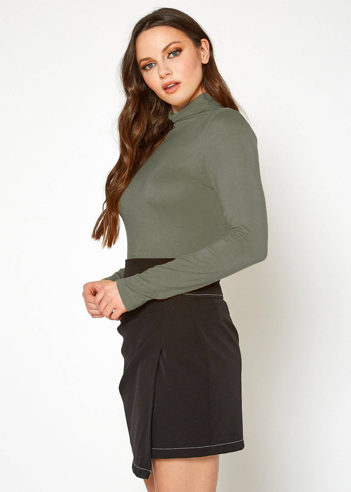 Olive-green turtle neck fitted top, model with long wavy brown hair posing against a white background.