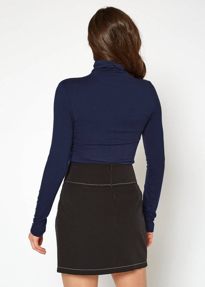 Form-fitting navy blue turtle neck top with long sleeves worn by a female model against a white background