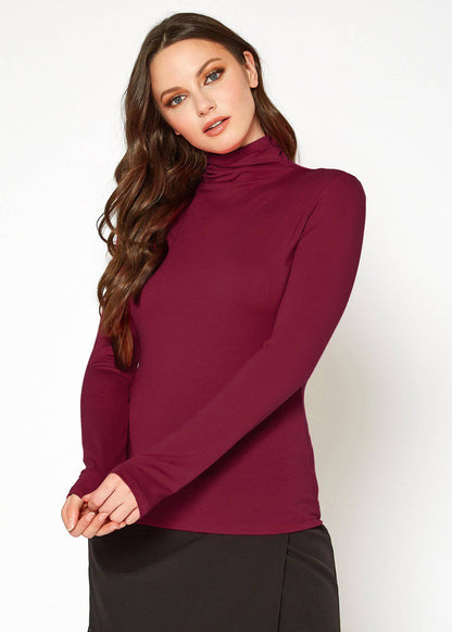 Woman's long-sleeve burgundy turtleneck fitted top with flowing curled hairstyle.