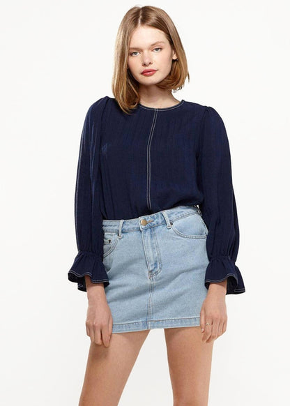 Navy blue puff shoulder top with bell cuff sleeves by Lemon Hera, worn with light denim mini skirt on a female model against a white background.