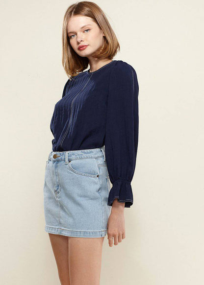 Navy blue women's puff shoulder top with bell cuff sleeves, showcased on a model wearing denim shorts against a neutral background.