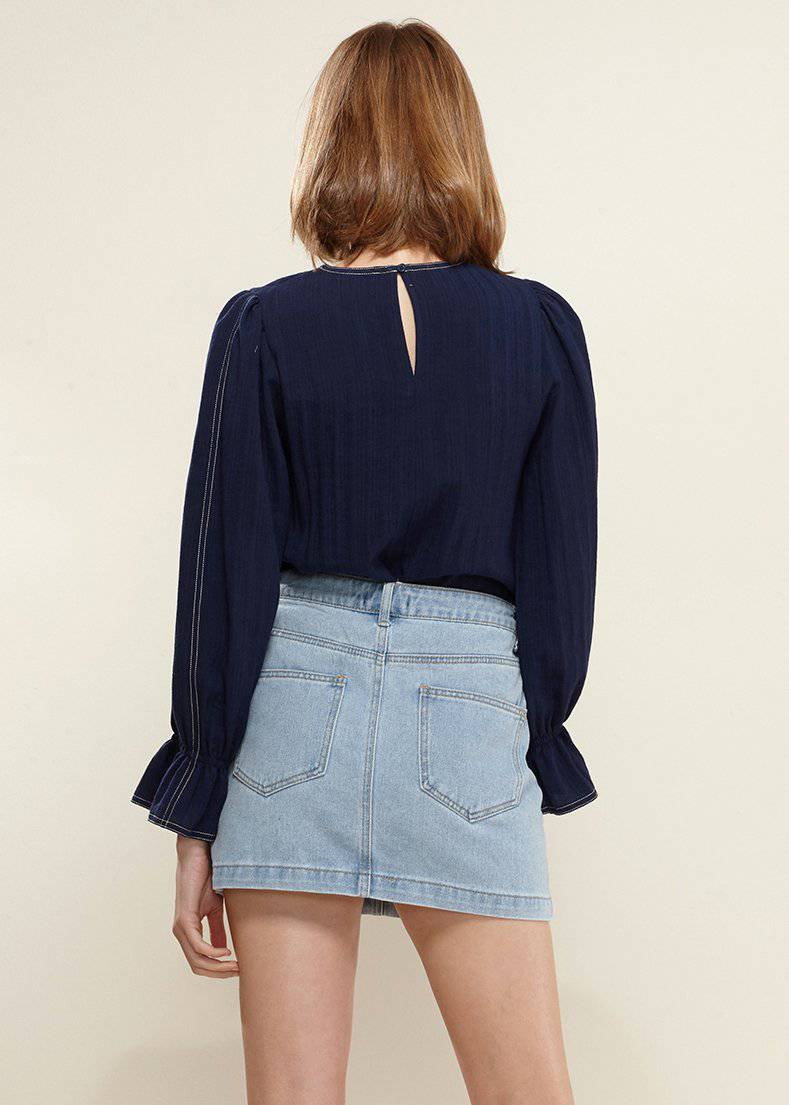 Navy blue women's blouse with puff shoulders and bell cuff sleeves, paired with a denim mini skirt.