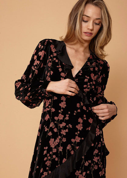 Floral velvet wrap dress with billowing sleeves, cinched waistline, and layered skirt in a dark romantic style, showcased on a female model against a beige background.