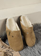 Cozy Suede Slippers on Plush Rug: Tan suede round-toe slippers with soft faux fur lining, sitting on a grey shaggy rug.