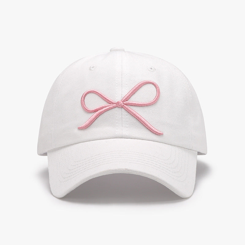 Elegant white cotton baseball cap with delicate pink bow embroidery, a stylish accessory for the fashion-conscious woman.