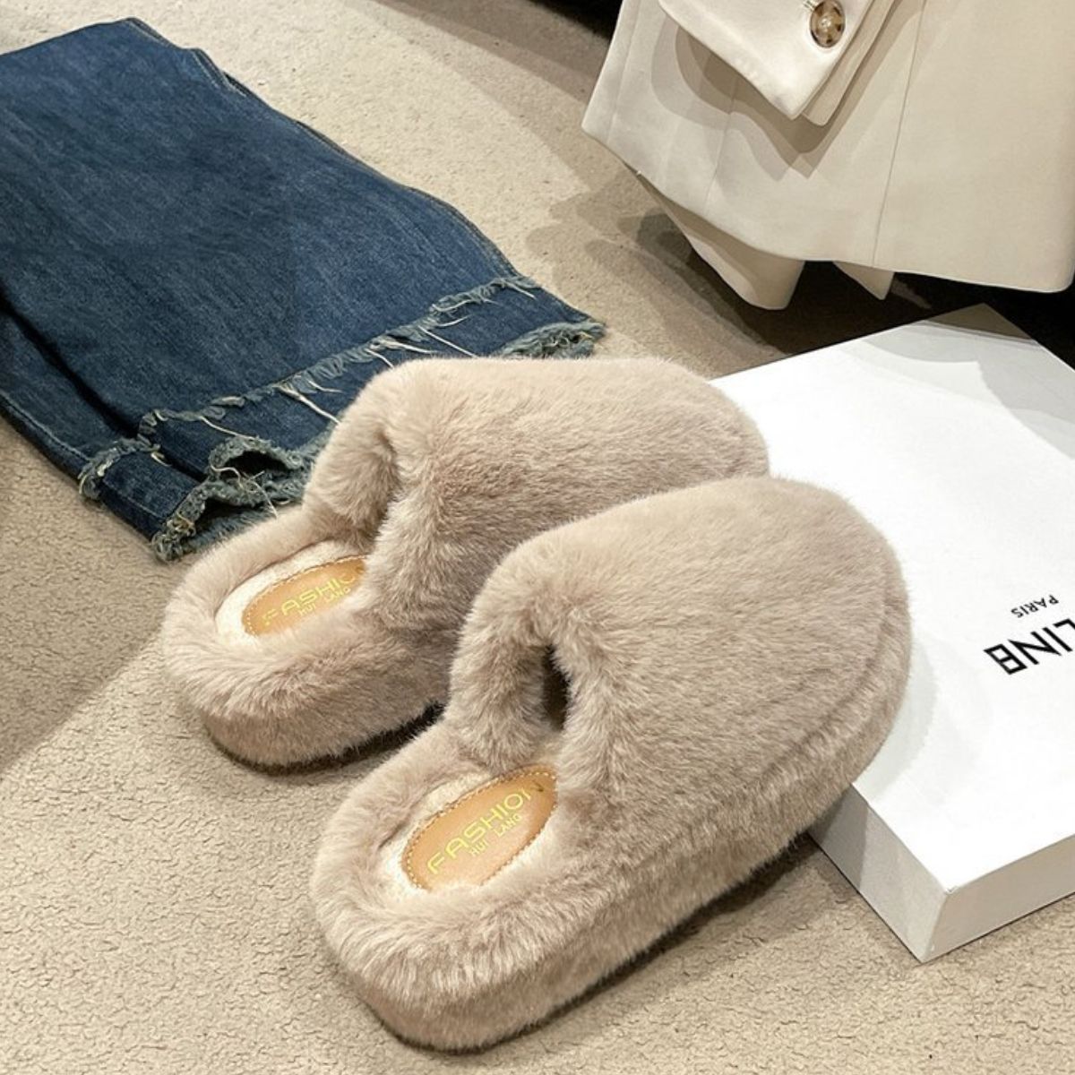 Soft, cozy beige fuzzy slippers on a hardwood floor with a pair of jeans in the background.