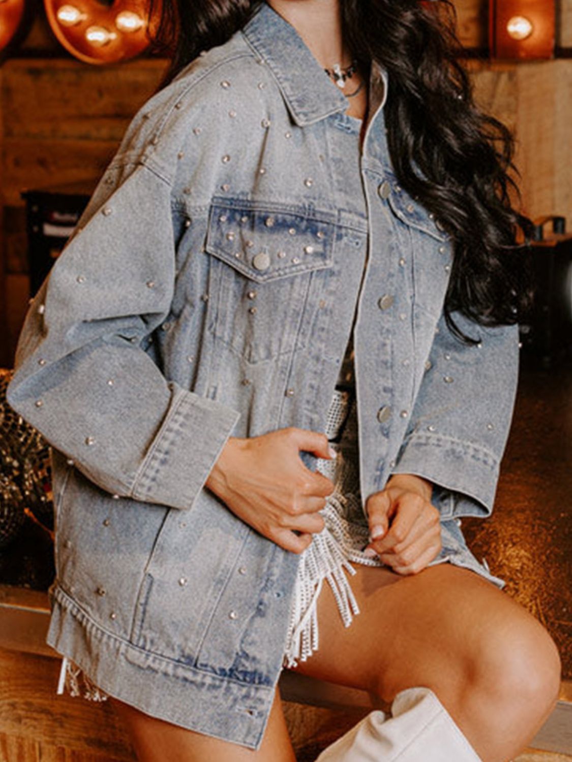 Stylish rhinestone embellished denim jacket with distressed detailing, showcased against a rustic wooden background.