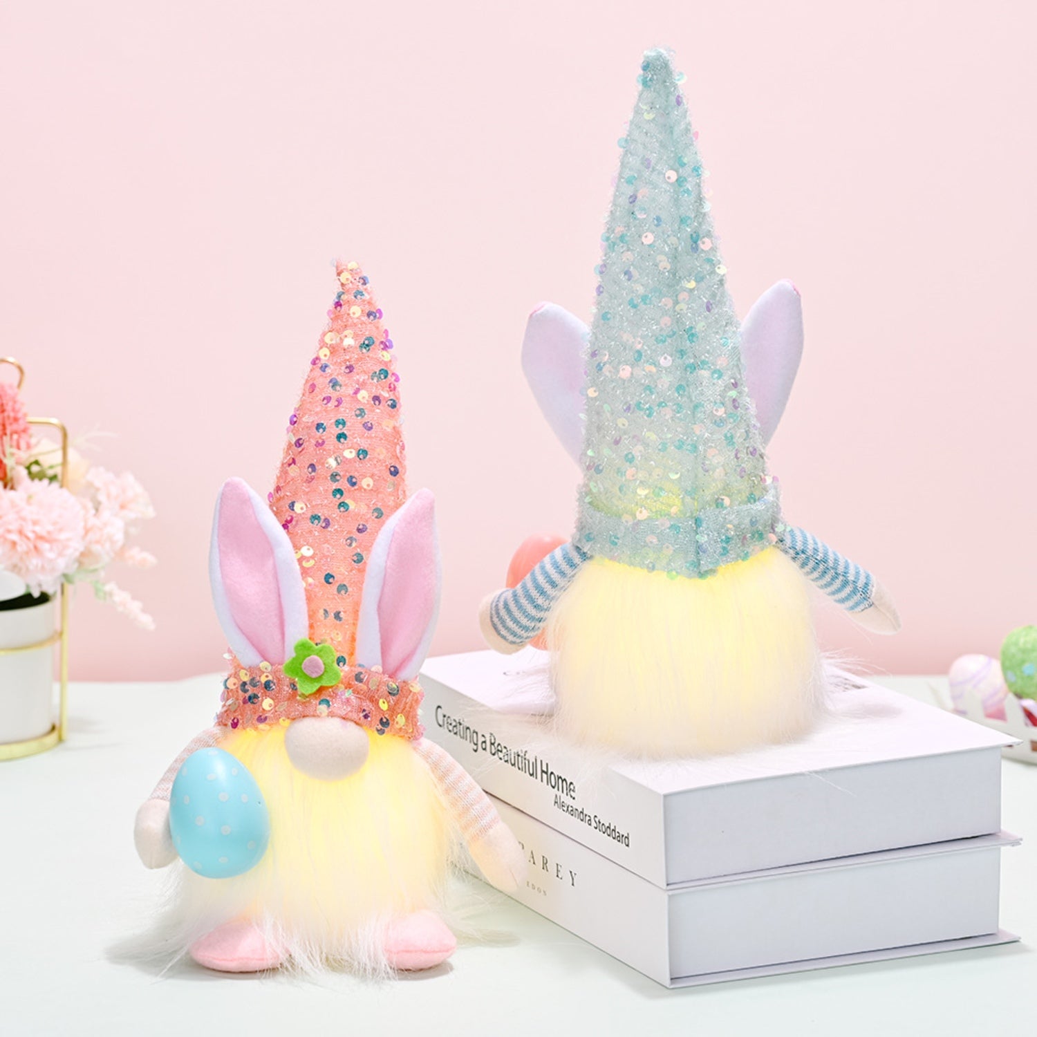 Whimsical Easter decor featuring pastel-colored sequined hats, a fluffy plush gnome figure, and floral accents on a light pink background.