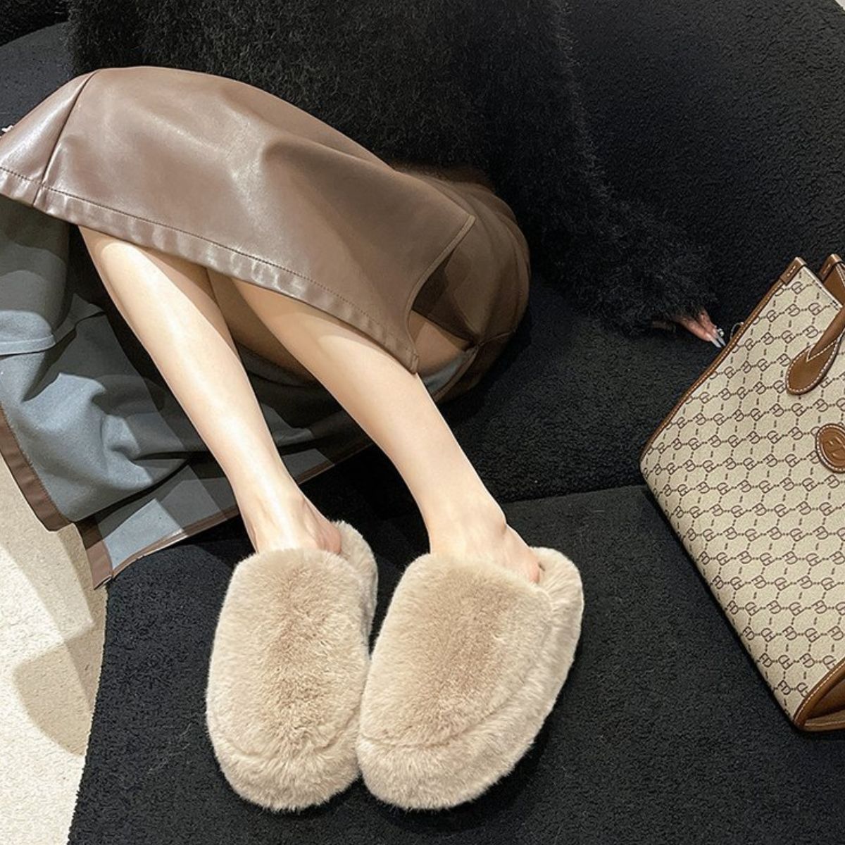 Plush beige slippers with round toe design, placed on a dark background alongside a designer handbag.