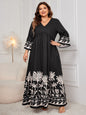 Elegant plus-size black and white printed maxi dress with long billowing sleeves and a v-neck design, showcased in a stylish indoor setting.