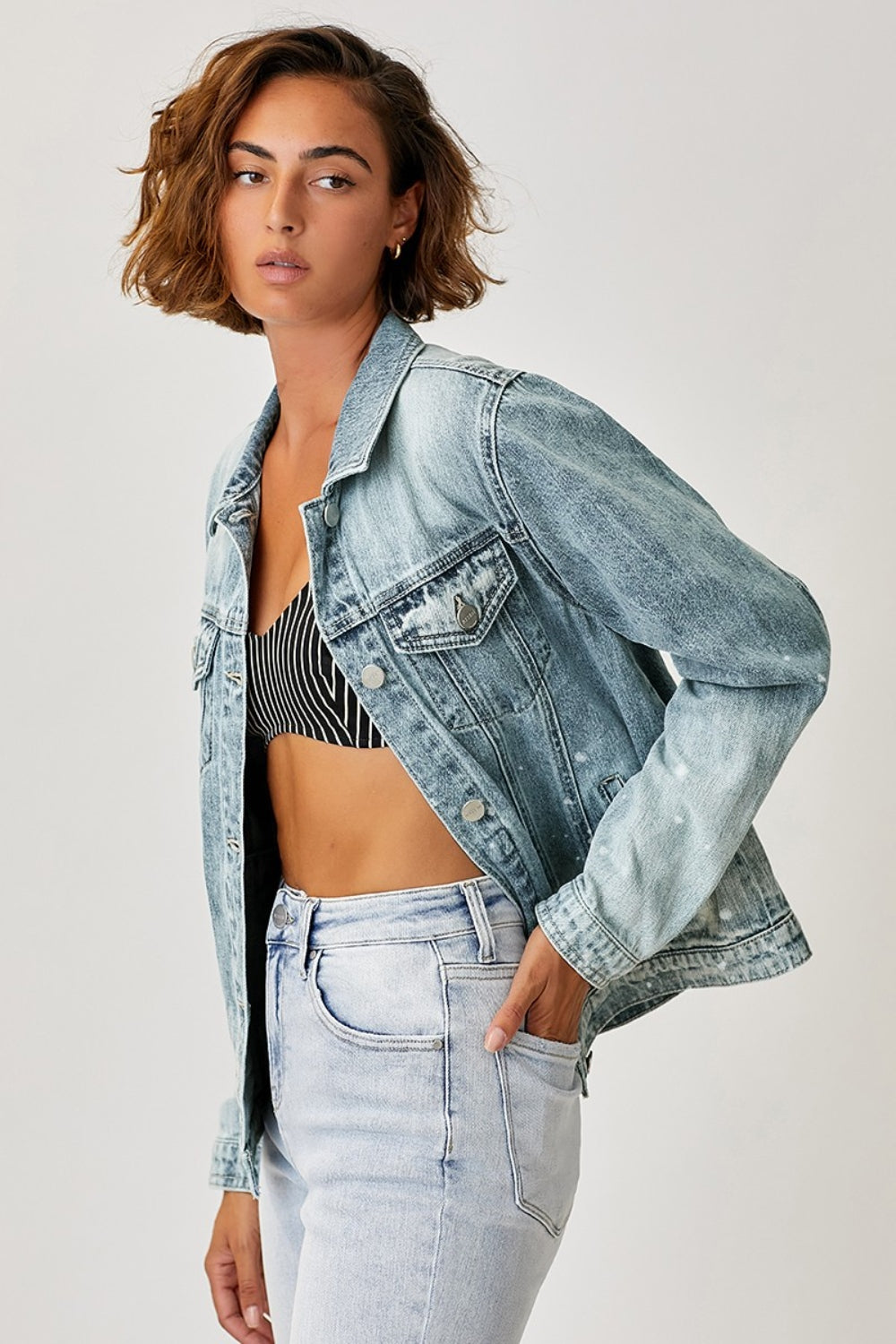 Stylish ombre-washed denim jacket with button-up design, worn by a woman with short wavy hair in a light-colored casual outfit.