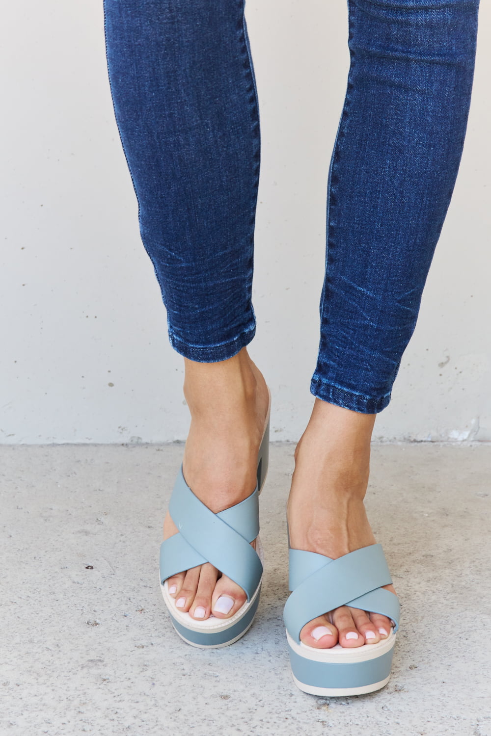 Misty blue contrast platform sandals on woman's feet against a white background