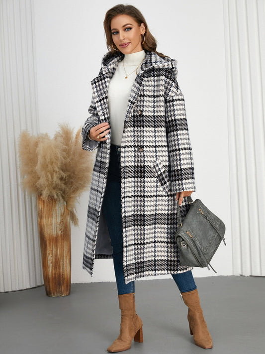 Elegant houndstooth plaid double-breasted longline coat with long sleeves, worn by a stylishly dressed woman with a handbag.