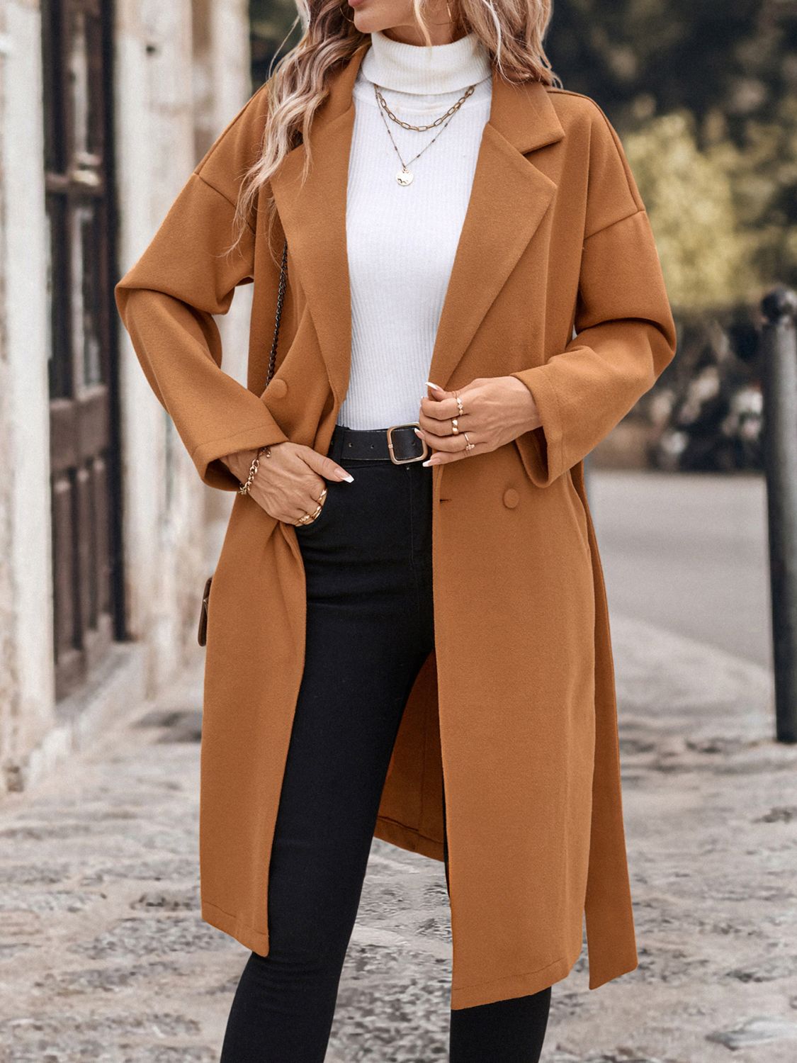 Stylish camel-colored wool coat with dropped shoulders and a tie waist, worn over a white top and black jeans, creating a classic and chic outfit for a winter day.