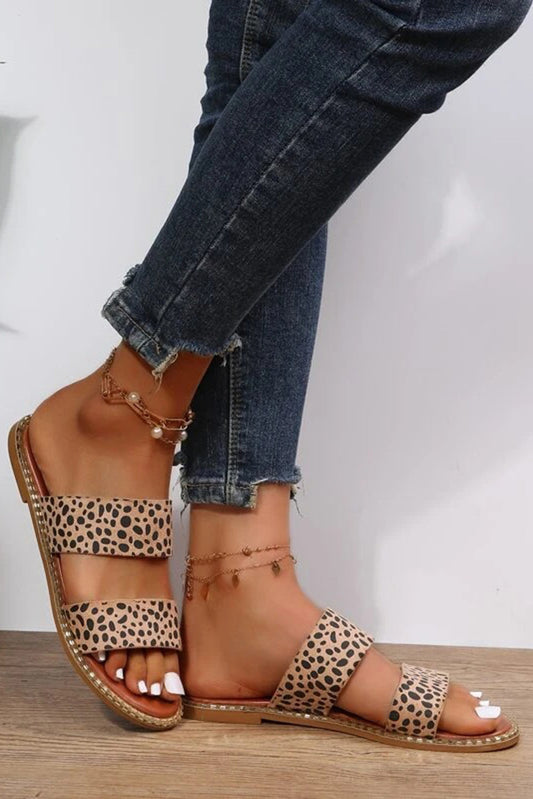 Leopard print double strap flat sandals on a woman's feet against a white background.