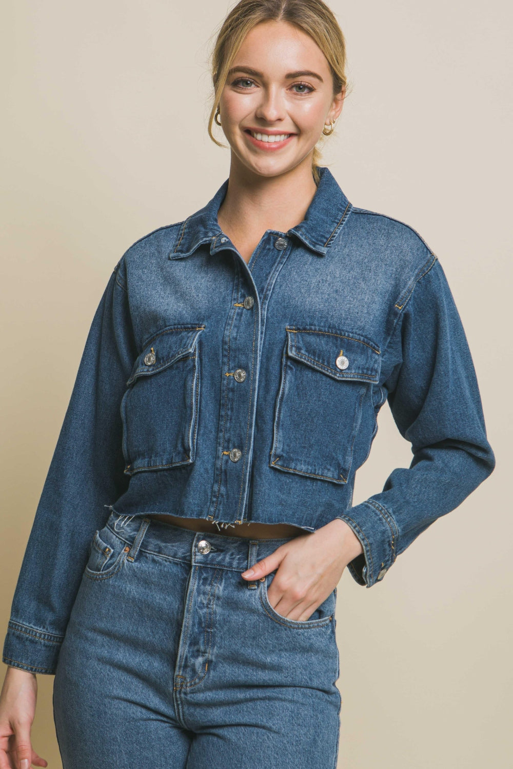 Stylish denim cropped jacket with raw hem and button-up closure, worn by a smiling young woman.