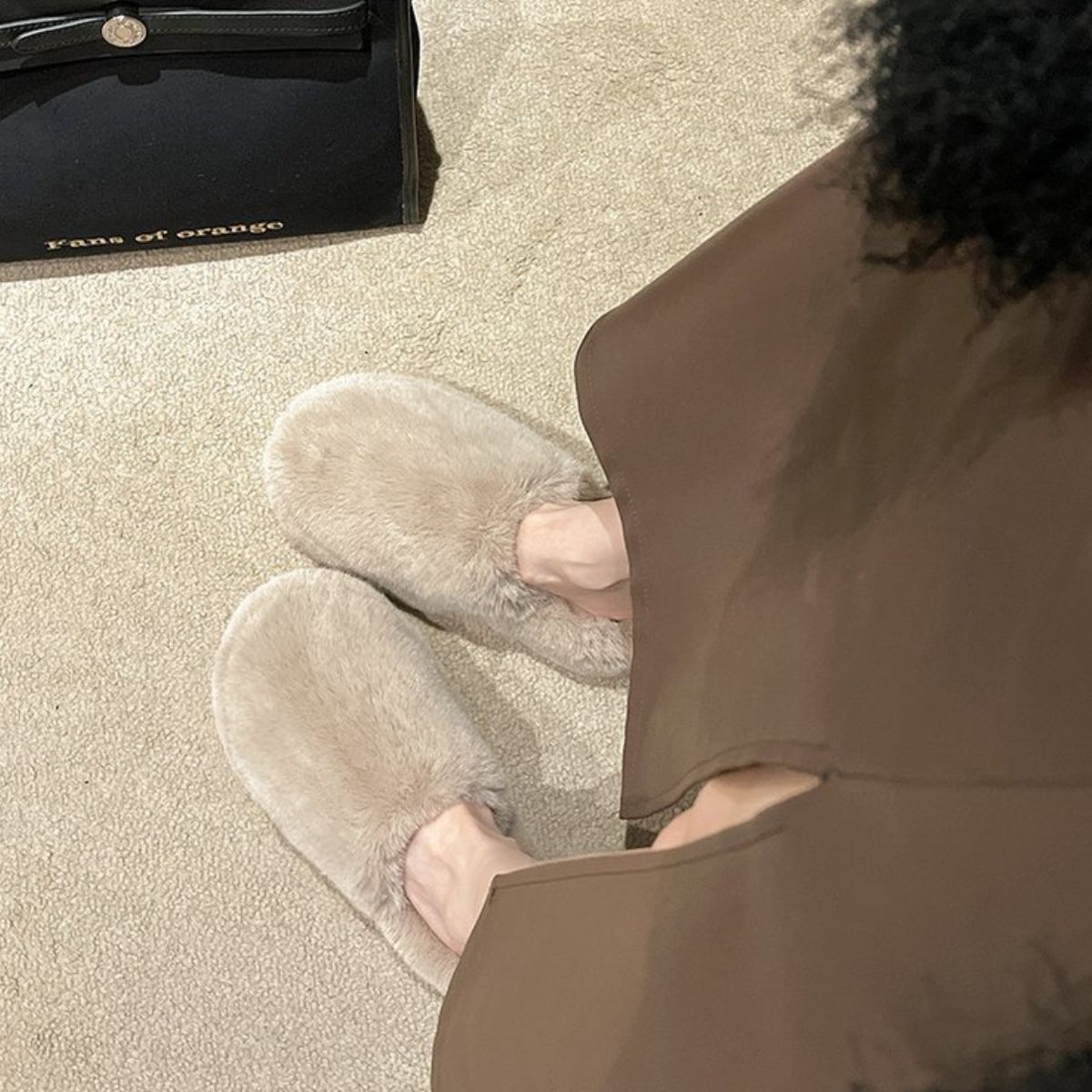 Soft, plush slippers resting on a light-colored rug near a leather bag