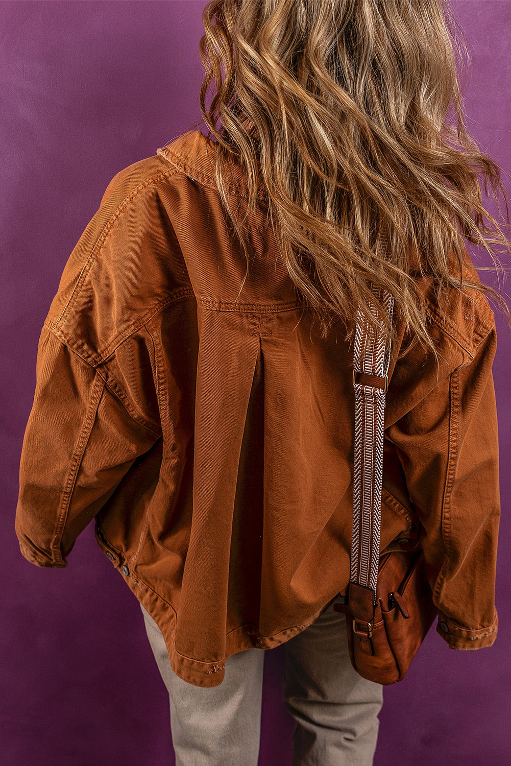 Textured Denim Jacket with Wavy Chestnut Hair
This image shows the back view of a person wearing a textured, burnt orange denim jacket. The jacket has a collared neckline and visible buttons down the center. The person's long, wavy chestnut-colored hair cascades over the jacket's shoulders.