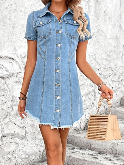 Denim dress with button-up front, short sleeves, and frayed hem, worn by a woman with long blonde hair standing in front of a stone wall