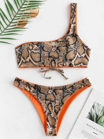 Tropical snake print one-shoulder bikini with orange trim, displayed on a white background with palm leaves.