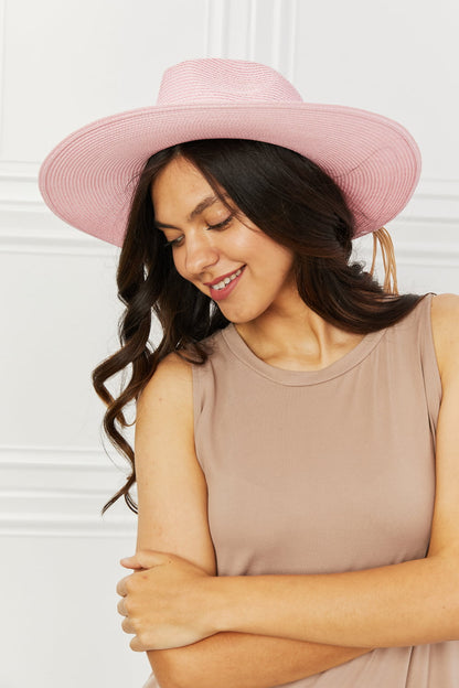 Elegant pink straw hat accenting a smiling woman's wavy dark hair in a beige top