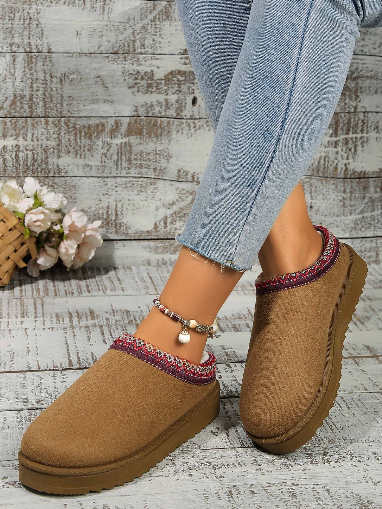 Cozy suede platform slippers with beaded details on a weathered wooden surface, surrounded by a flower bouquet.