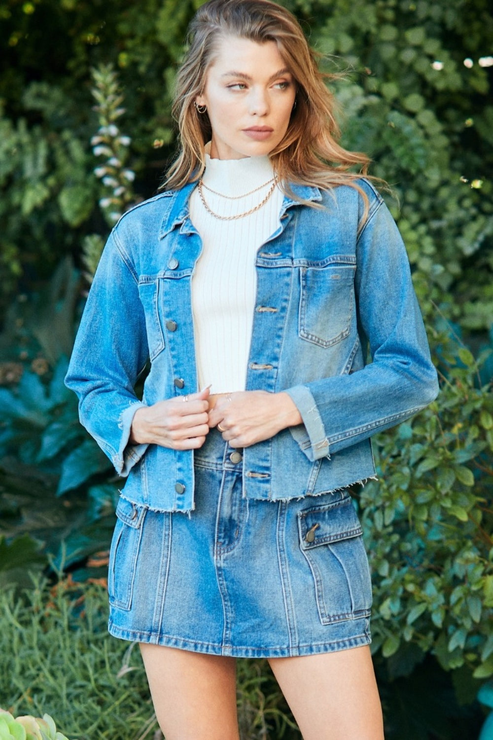 Stylish denim jacket with raw hem adorning a model in a natural, lush setting.