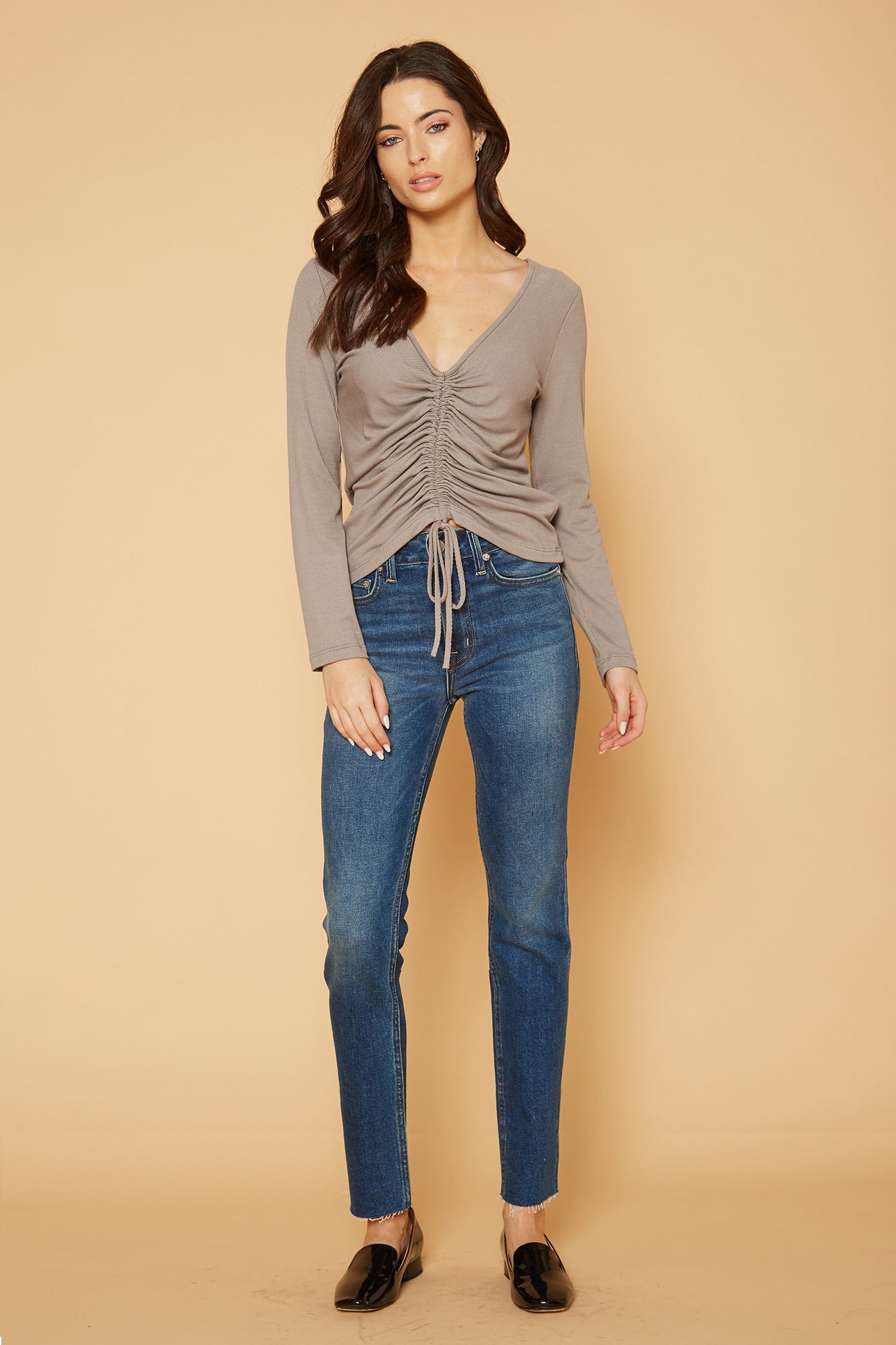 Elegant woman's V-neck ruched top in coco, paired with classic blue jeans, creating a stylish casual look.