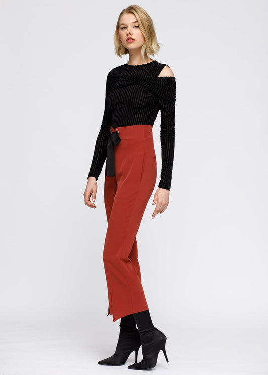 Stylish black velvet open-shoulder top with bold red high-waisted pants, complemented by chic ankle boots, creating an elegant and modern fashion ensemble.