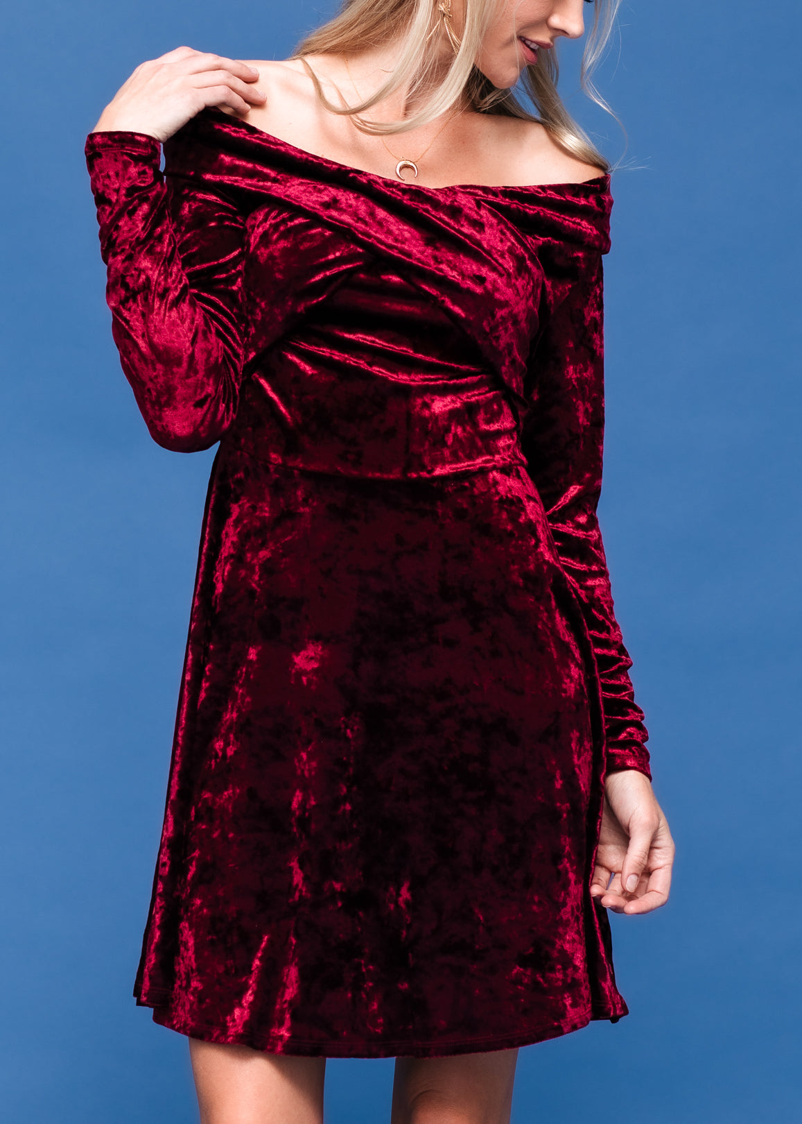 Elegant velvet off-shoulder dress, deep burgundy color, flared skirt, fashion model posing against blue background.