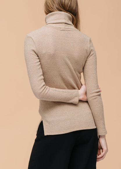 Soft beige turtleneck sweater top with ribbed knit texture, showcased on a female model against a neutral background.