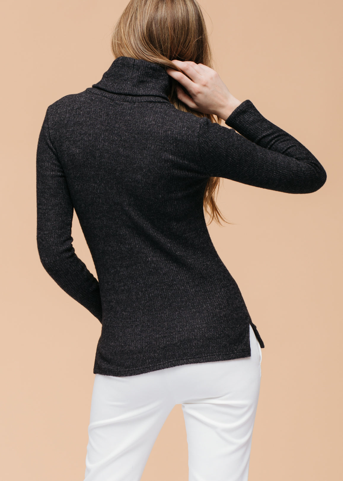 Cozy black ribbed knit sweater with a high turtleneck, shown on a woman from the back, posing against a neutral beige background.