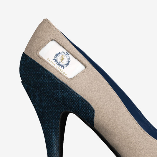 Elegant navy blue and beige high-heeled shoe from the Sasha London Alilyah Heel collection. The pointed toe design and embroidered logo detail add a touch of sophistication.