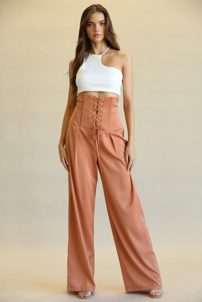 High-waist laced orange trousers worn by a young woman with long dark hair against a beige background.