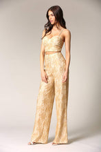 Load image into Gallery viewer, Golden lace pant suit with flared legs, worn by a woman with long dark hair and a sleeveless top, standing on a plain background.